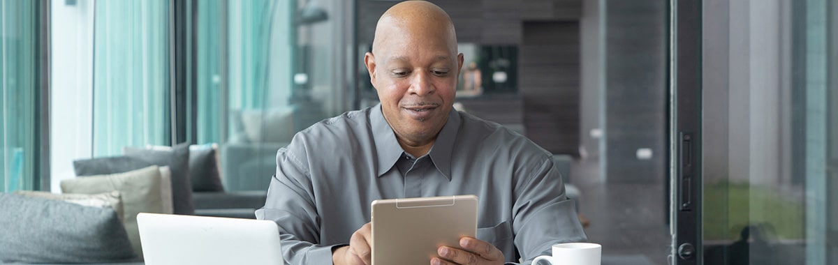 Senior citizen working from home on table with tablet and laptop computer